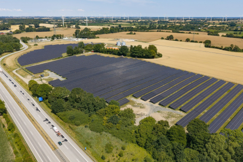 Luftbild eines Solarparks neben der Autobahn A1 bei Lensahn mit Windpark am Horizont