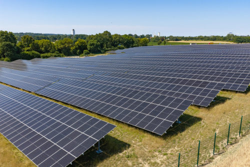 Luftbild von Solarmodulreihen mit Sicherheitszaun und Wasserturm im Hintergrund