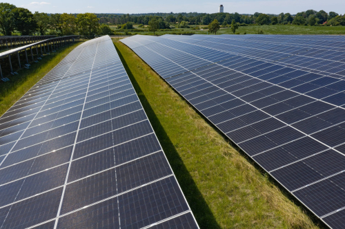 Luftbild von Solarmodulreihen mit Grasstreifen und Wasserturm im Hintergrund