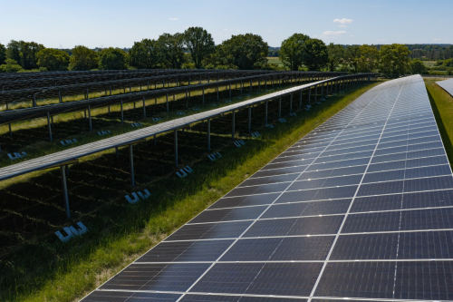 Luftaufnahme aufgeständerter Solarmodule mit sichtbaren Fundamenten und Bewuchs