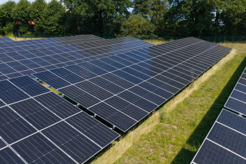 Luftaufnahme von Solarmodulreihen am Rand der Anlage mit Zaun und Baumbestand